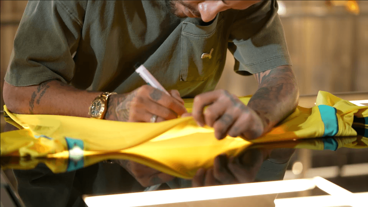 Neymar Jr. assinando uma camiseta amarela da Seleção Brasileira